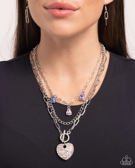 <p>Three mismatched silver chains layer and loop around the neckline. A purple, light pink, and blue teardrop gem in silver-pronged fittings dangle from the uppermost chain while an iridescent-rhinestone encrusted heart pendant loops through the lowermost chain for a radiantly, romantic statement. Features an adjustable clasp closure. Due to its prismatic palette, color may vary.</p> <p><i> Sold as one individual necklace. Includes one pair of matching earrings.</i></p>