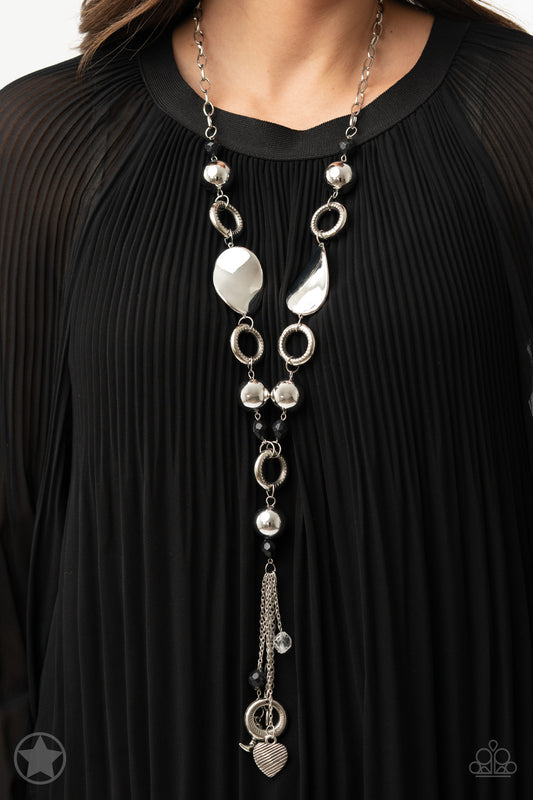 Long chain of black crystalized beads, curved plates of silver with a pearly finish, and chunky silver rings lead down to a tassel of chains and charms, including a crescent moon and a heart.  Sold as one individual necklace. Includes one pair of matching earrings.