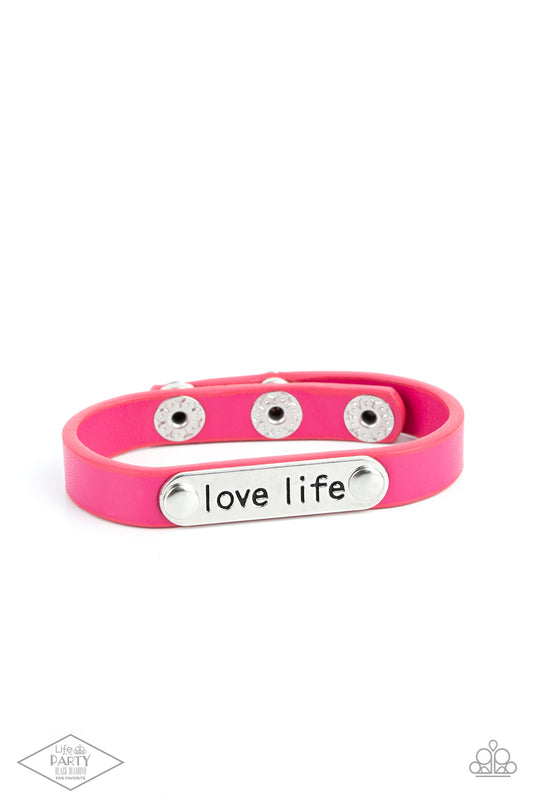 A silver plate engraved with the inspirational phrase “love life” is studded in place along a skinny strip of pink leather. Brushed in a shiny finish, the dainty band wraps around the wrist in a colorfully seasonal style. Features an adjustable snap closure.  Sold as one individual bracelet.