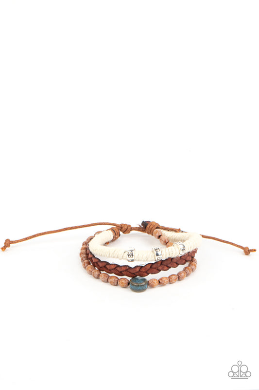 Featuring floral stamped accents and a colorful ceramic-like bead, strands of wooden beads, white twine, and braided leather layer around the wrist for an earthy look. Features an adjustable sliding knot closure.  Sold as one individual bracelet.