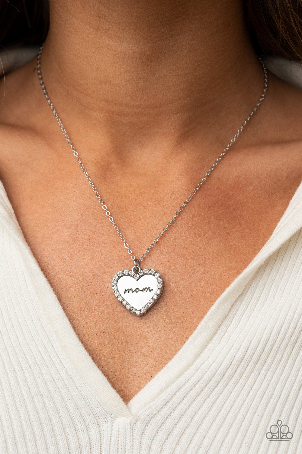 Infused with a glassy white rhinestone encrusted silver heart, a silver heart shaped pendant is stamped in the word, "Mom," as it swings below the collar, creating a sparkly sentimental statement piece. Features an adjustable clasp closure.  Sold as one individual necklace. Includes one pair of matching earrings.