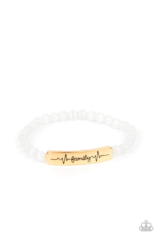 Stamped in heartbeats and the word, "Family," a glistening gold plate attaches to a strand of white cat's eye stone beads that are threaded along a stretchy band, creating a whimsically sentimental centerpiece around the wrist.  Sold as one individual bracelet.
