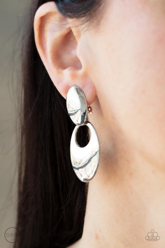 An oversized beveled silver hoop swings from the bottom of a shiny silver fitting, creating an edgy refinement. Earring attaches to a standard clip-on fitting.  Sold as one pair of clip-on earrings.   Clip On Earring