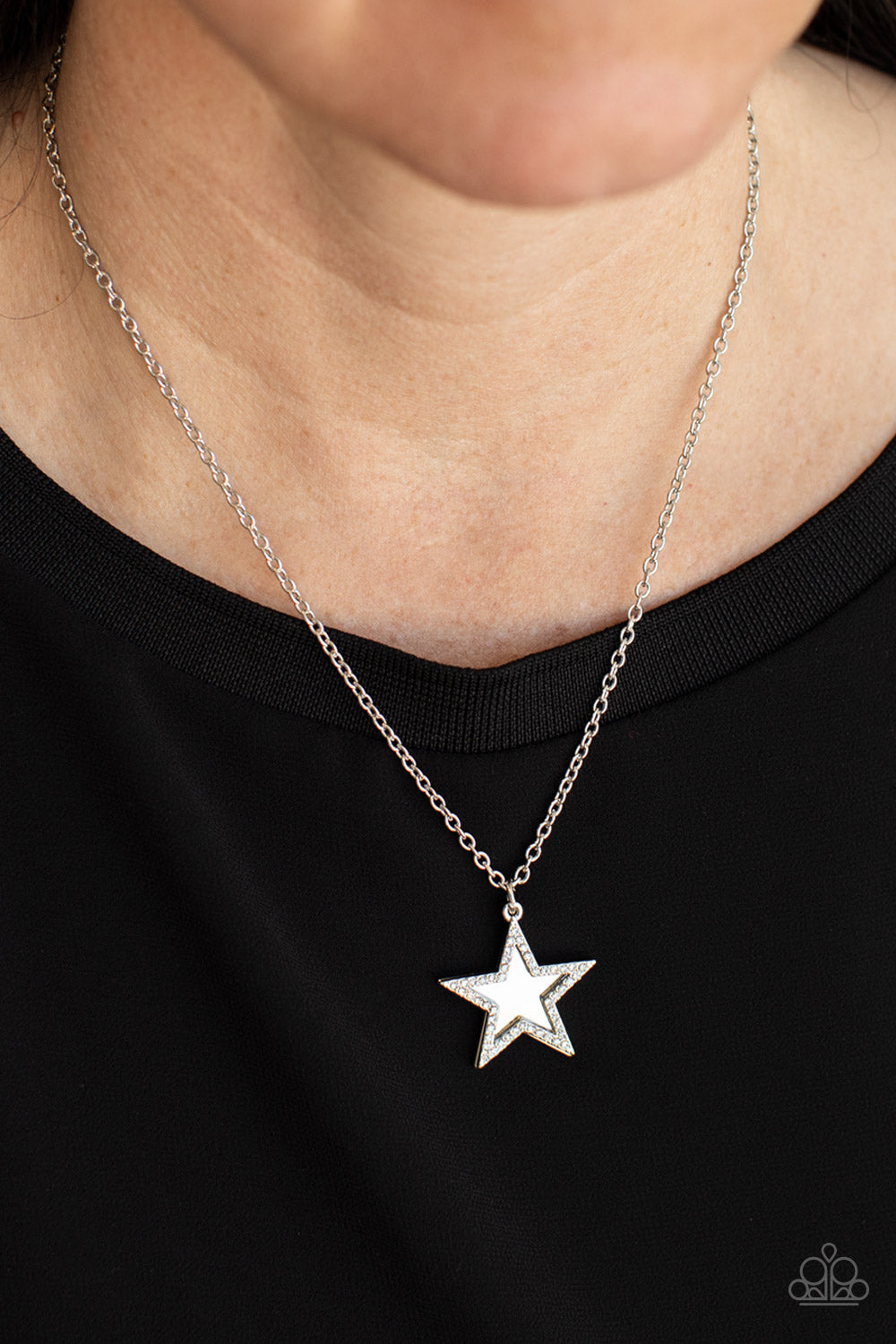 A white rhinestone encrusted silver star delicately overlaps with a shiny silver star below the collar, creating a sparkly patriotic pendant. Features an adjustable clasp closure.  Sold as one individual necklace. Includes one pair of matching earrings.