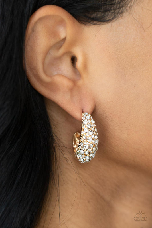 Featuring a beveled surface, a thick hammered gold hoop is haphazardly encrusted in round and square white rhinestones for a glamorously glittery finish. Earring attaches to a standard post fitting. Hoop measures approximately 3/4" in diameter.  Sold as one pair of hoop earrings.