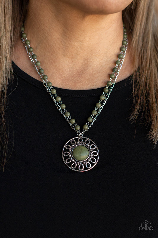 A dainty silver chain is paired with a grounding green stone beaded chain below the collar. An oversized green stone adorns the center of an antiqued silver frame radiating with silver studded and wire-like detail, creating an authentic artisan inspired pendant at the bottom of the earthy chains. Features an adjustable clasp closure.  Sold as one individual necklace. Includes one pair of matching earrings.