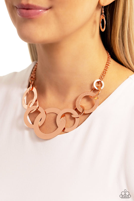 A shiny collection of flat copper rings in varying sizes and brushed in a brilliant coppery shimmer, link together below the collar. The assortment of copper rings attaches to a bright copper chain for a dazzling finish. Features an adjustable clasp closure.  Sold as one individual necklace. Includes one pair of matching earrings.