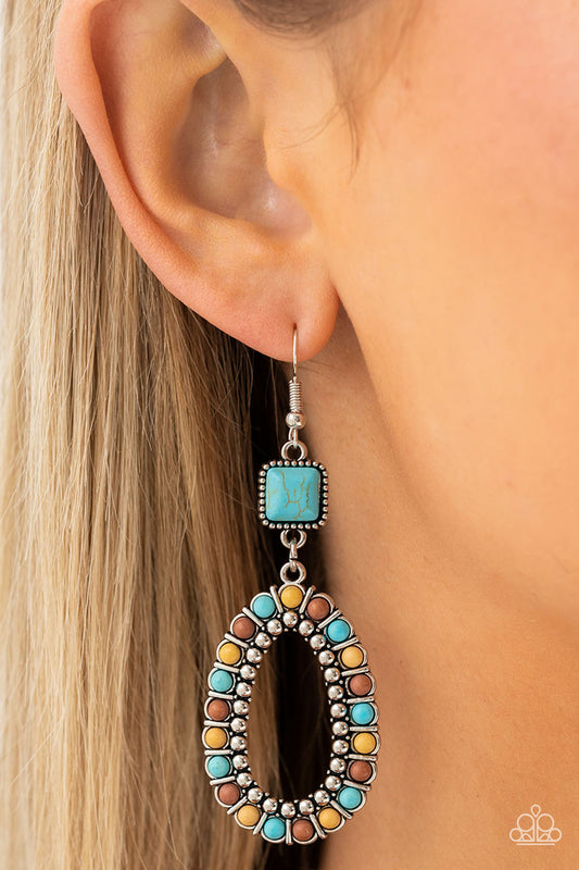 A turquoise stone, chiseled into a polished square, gives way to a silver studded hoop bordered in dainty turquoise, brown, and yellow stones, creating a rustically scalloped lure. Earring attaches to a standard fishhook fitting.  Sold as one pair of earrings.