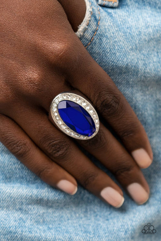 Bordered by a glitzy ring of white rhinestones, an oblong blue gem embellishes the center of a dramatically oversized silver frame for a blinding finish. Features a stretchy band for a flexible fit.  Sold as one individual ring.