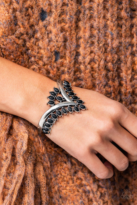 Black oval stones, encased in studded silver frames, line the edge of a daring V-shaped silver cuff. A gathering of black stones adorns the center of the bracelet, adding a finishing touch to the rustically regal cuff.  Sold as one individual bracelet.