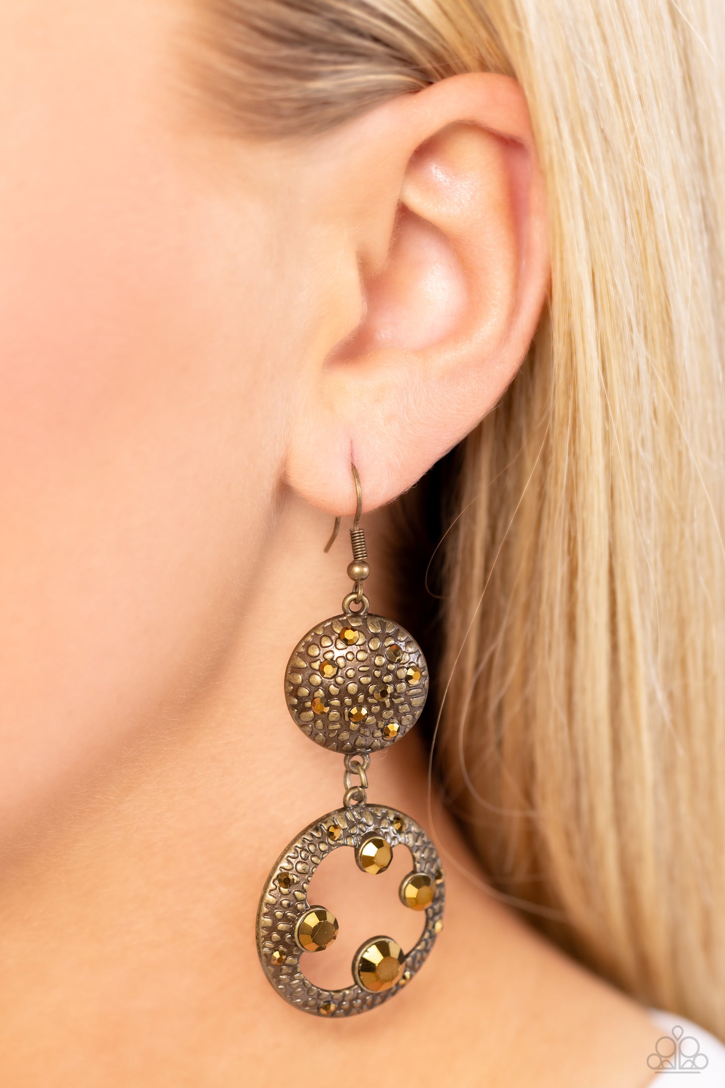 Dotted with dainty aurum rhinestones and embossed in pebble-like textures, a beveled brass circle attaches to an imperfect brass hoop featuring matching texture. A smattering of oversized aurum rhinestones haphazardly adorns the hoop, resulting in a gritty shimmer. Earring attaches to a standard fishhook fitting.  Sold as one pair of earrings.