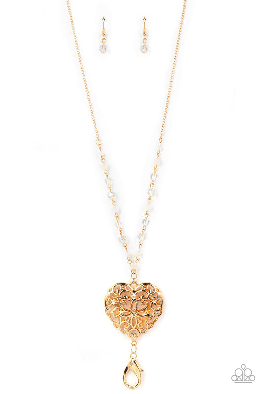 A dainty collection of opaque, glassy, and crystal-like beads give way to an oversized filigree filled heart frame, creating an antiqued locket inspired pendant at the bottom of a lengthened gold chain. A lobster clasp hangs from the bottom of the design to allow a name badge or other item to be attached. Features an adjustable clasp closure.  Sold as one individual lanyard. Includes one pair of matching earrings.