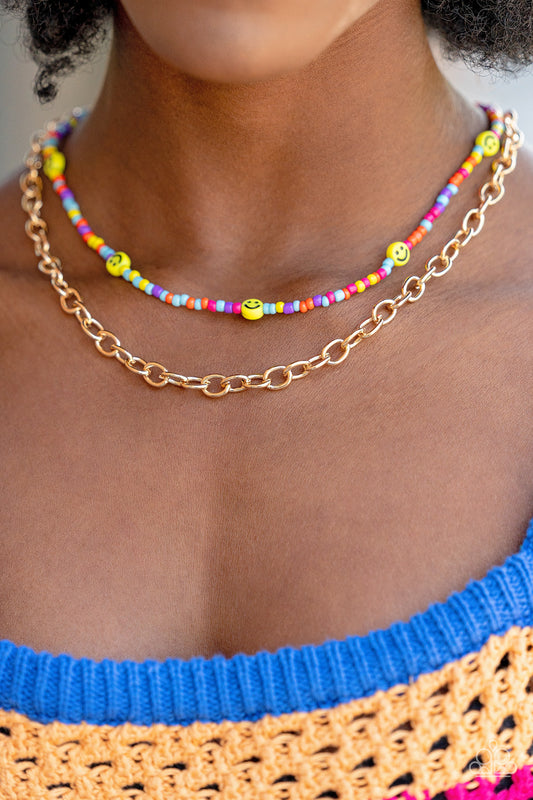 Layered together with a bold gold chain, dainty multicolored seed beads and yellow smiley face beads are threaded along an invisible wire below the collar, resulting in a colorfully retro design. Features an adjustable clasp closure.  Sold as one individual necklace. Includes one pair of matching earrings.