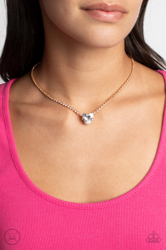 An oversized white heart-shaped gem, set in an airy, pronged gold fitting, glitters at the center of a blinding row of dainty, glassy white rhinestones set in square gold fittings, resulting in a flirtatious sparkle around the neckline. Features an adjustable clasp closure.  Sold as one individual choker necklace. Includes one pair of matching earrings.  New Kit Choker Get The Complete Look! Bracelet: "Bedazzled Beauty - Gold" (Sold Separately)