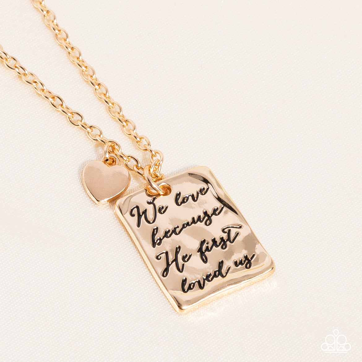 Dangling from a delicate gold chain, a hammered rectangular plate swings for eye-catching movement. The religious phrase "We love because he first loved us" prominently stands out in the center, in an antiqued font. A gold heart charm glides just above the rectangular plate for a vintage-inspired finish. Features an adjustable clasp closure.  Sold as one individual necklace. Includes one pair of matching earrings.