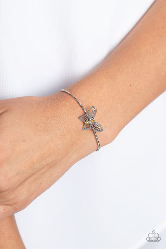 A deceptively simple silver butterfly charm glides along a silver snake chain for a whimsical flair along the wrist. Dainty, yellow rhinestones, brushed in a UV shimmer, encrust along the butterfly's body, creating an understated shimmer, while intricate, airy wings fold out from the sparkle, adding a 3D effect to the design. Features an adjustable sliding knot closure. Due to its prismatic palette, color may vary.  Sold as one individual bracelet.