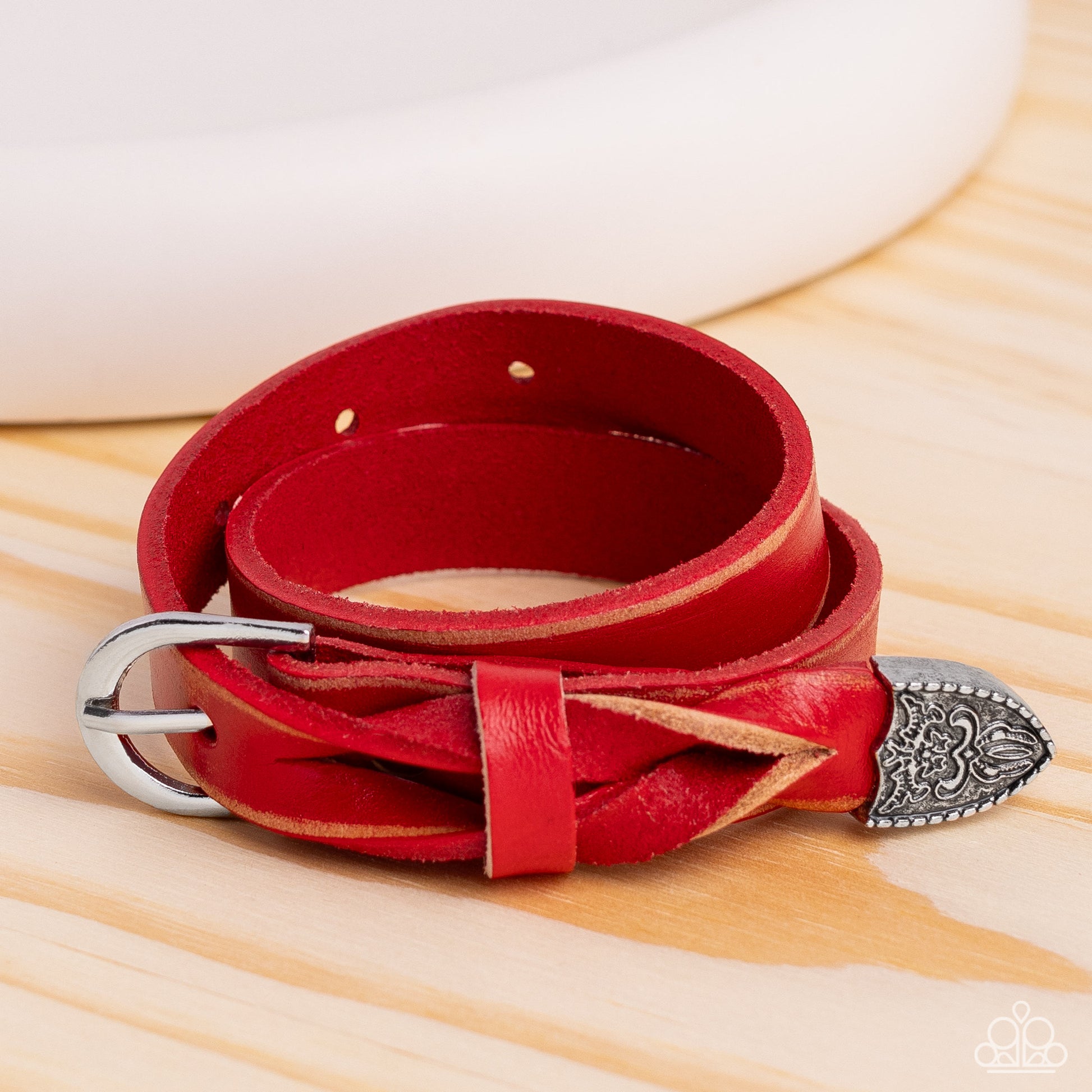 Featuring a weathered finish, a red leather band loops around the wrist in a belt loop fashion. Featured at the end of the loop, the leather braids into a silver cap fitting, embossed with a coat of arms style filigree for an urban statement. Features an adjustable belt loop closure.   Featured inside The Preview at Made for More! Sold as one individual bracelet.