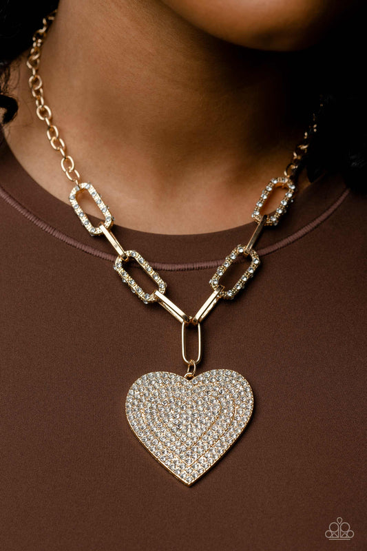Elongated, oversized gold links, encrusted with a blinding display of white rhinestones and shimmery gold accents connect a classic gold chain to an exaggerated gold heart pendant for a romantically refined finish. Featured on the oversized gold heart, layers upon layers of glitzy white rhinestones emboss across its entire surface as the hearts gradually increase in size from the center. Features an adjustable clasp closure.  Sold as one individual necklace. Includes one pair of matching earrings.