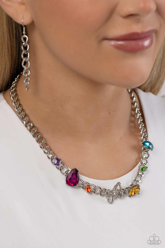 A succession of various gleaming, multicolored gems encased in silver fittings are affixed to a high-sheen, thick silver curb chain, adding dramatic dimension and color to an industrial statement. An airy silver butterfly frame adorned in white rhinestones is featured on the center of the silver curb chain for a touch of whimsicality. Features an adjustable clasp closure.  Sold as one individual necklace. Includes one pair of matching earrings.