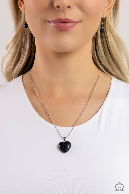 Brushed in a glittery finish, a dark blue heart dangles at the bottom of a lengthened silver snake chain, creating a glittery pendant. Features an adjustable clasp closure.  Sold as one individual necklace. Includes one pair of matching earrings.