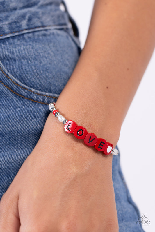 Infused on an elastic stretchy band, white pearls, red seed beads, silver studs, and red beads spelling out the word "LOVE" with a white heart bead aside it wraps around the wrist for a sentimental, youthful display.  Sold as one individual bracelet.